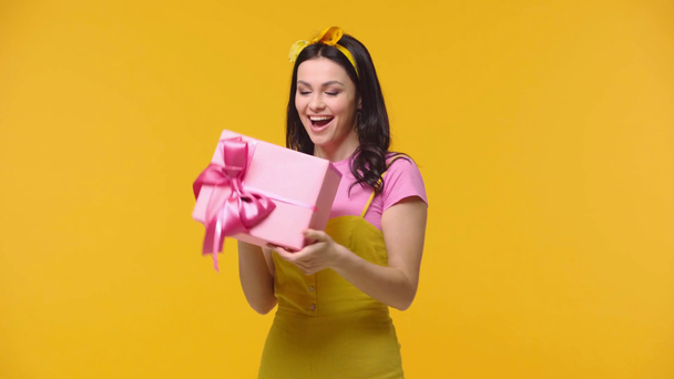 Frau schüttelt Geschenkbox und lächelt isoliert auf gelb - Filmmaterial, Video