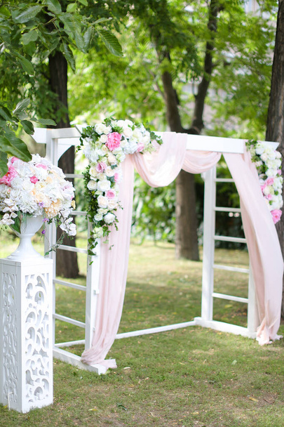 Łuk ślubny, ozdobiony niesamowitymi różami i krzesłami w parku. - Zdjęcie, obraz