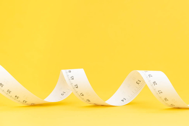White paper measuring tape roll on solid yellow background with copy space using as nutrition diet, tailer designer or measure tool for furniture design. - Foto, afbeelding