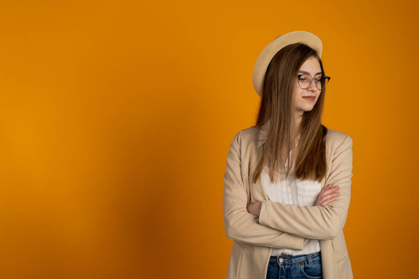 Girl in hat and glasses posing with crossed arms on yellow background - Fotografie, Obrázek