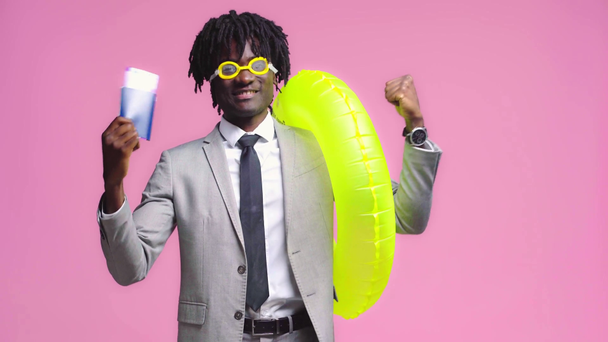 Αφροαμερικάνος με αεροπορικό εισιτήριο και φουσκωτό δαχτυλίδι απομονωμένο σε ροζ - Πλάνα, βίντεο