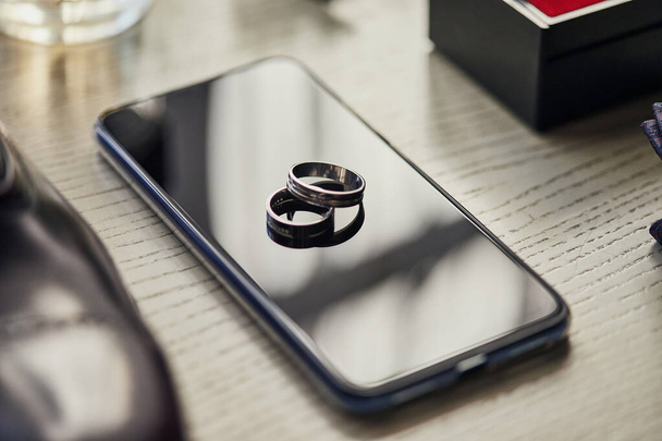 Los anillos de boda están en el teléfono. Los accesorios diferentes del empresario para la creación del estilo de las personas sobre el fondo de madera - Foto, Imagen