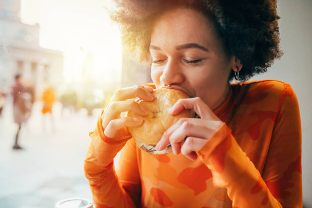 Fiatal gyönyörű többnemzetiségű nő eszik hamburger - éhező, finom, elégedettség koncepció - Fotó, kép