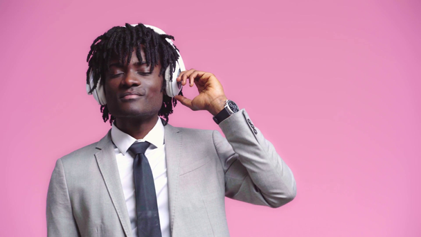 Afrykański amerykański biznesmen tańczący ze słuchawkami odizolowanymi na różowo - Materiał filmowy, wideo
