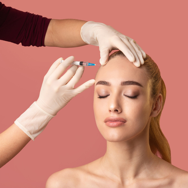 vrouw het krijgen van schoonheid injectie in voorhoofd gladstrijken huid, roze achtergrond - Foto, afbeelding