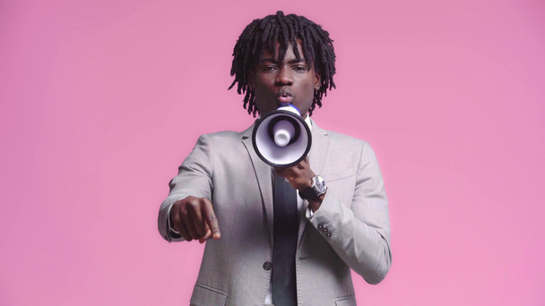 Irritated african american businessman speaking in loudspeaker isolated on pink - Footage, Video