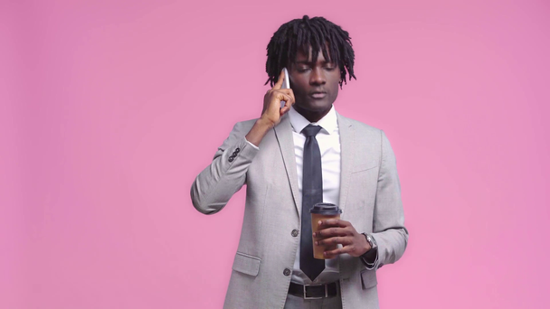 Hombre de negocios afroamericano con café hablando en gadget aislado en rosa
 - Imágenes, Vídeo