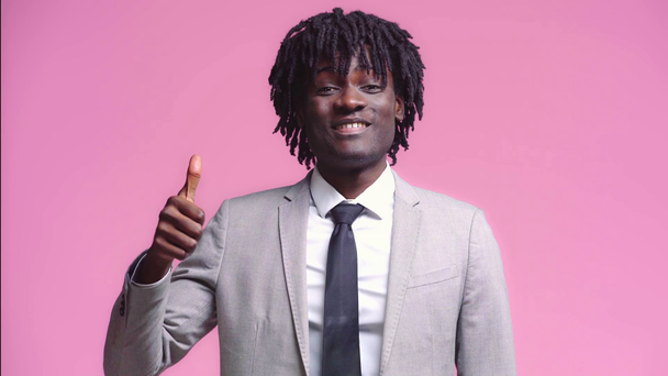 Hombre de negocios afroamericano sonriendo con el pulgar hacia arriba aislado en rosa
 - Imágenes, Vídeo