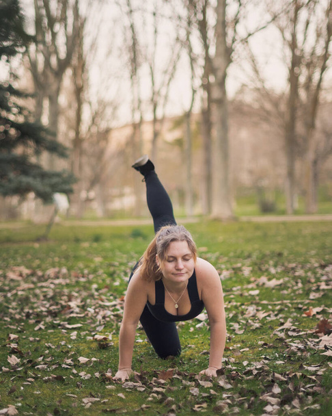 young blonde girl with blue eyes and black outfit doing outdoors exercises in a park on a warm winter afternoon - Photo, Image