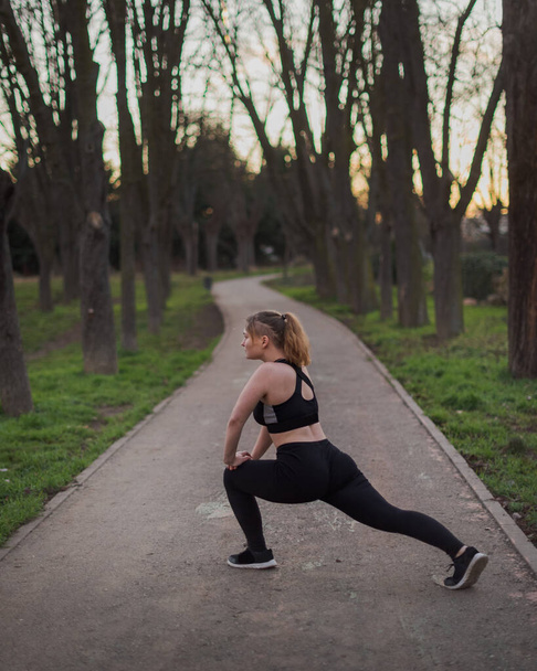 young blonde girl with blue eyes and black outfit doing outdoors exercises in a park on a warm winter afternoon - Photo, Image
