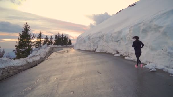 Sebevědomá běžkyně běžící po asfaltové cestě odrážející zlatý západ slunce v horách - Záběry, video
