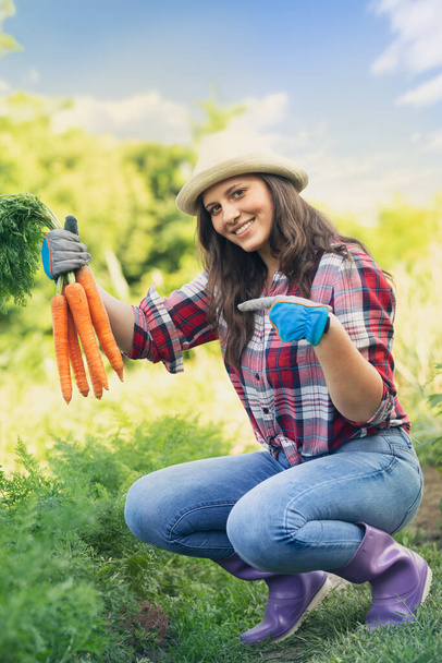 Beautiful smiling young woman holding carrots freshly picked - Valokuva, kuva