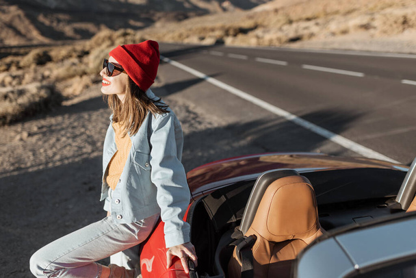 Woman traveling by the red car on a desert road - Φωτογραφία, εικόνα