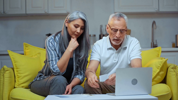 ηλικιωμένο διαφυλετικό ζευγάρι ψάχνει λογαριασμούς κοντά στο laptop  - Πλάνα, βίντεο