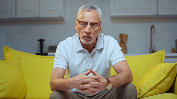 Senior mit Brille gestikuliert und redet im Wohnzimmer  - Filmmaterial, Video