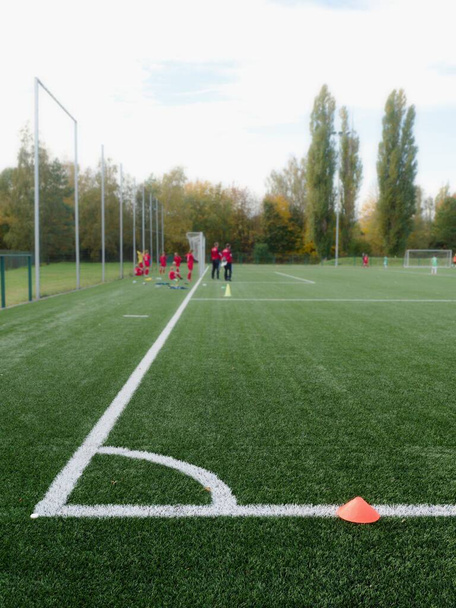Выборочный фокус на конусы, используемые для футбольных тренировок на зеленой искусственной территории с расплывчатыми игроками ребенка тренировки фон
 - Фото, изображение