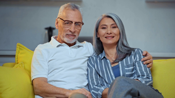happy senior and interracial couple hugging in living room  - Filmati, video