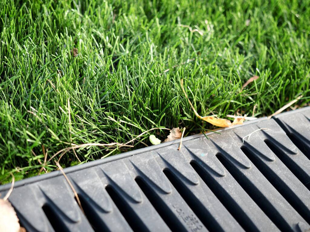Drainage systems. Storm taps.  Concrete and metal construction between pavement and green. Sewer and grate on the ground for draining water closeup. - Photo, Image