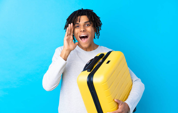 Jovem viajante afro-americano segurando uma mala gritando com a boca bem aberta
 - Foto, Imagem