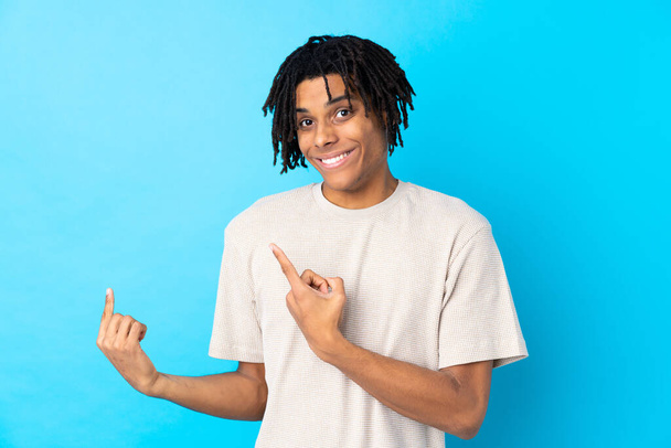 Young African American man over isolated blue background frightened and pointing to the side - Fotografie, Obrázek