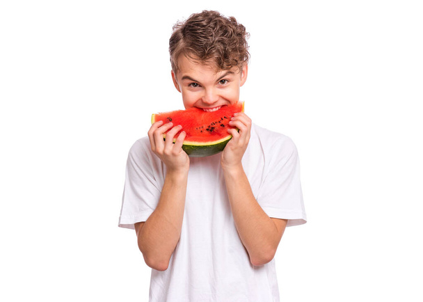 Portrait of teen boy eating ripe juicy watermelon and smiling. Cute caucasian young teenager with slice healthy watermelon. Funny happy child wearing white t-shirt, isolated on white background. - Foto, Imagen