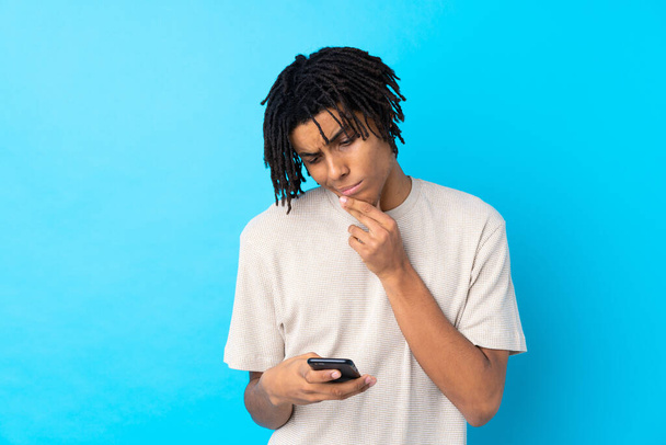 Молодой афроамериканец на изолированном синем фоне думает и посылает сообщение
 - Фото, изображение