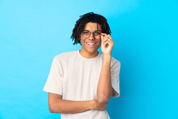 Νεαρός Αφροαμερικανός πάνω από απομονωμένο μπλε φόντο με γυαλιά και χαρούμενος - Φωτογραφία, εικόνα