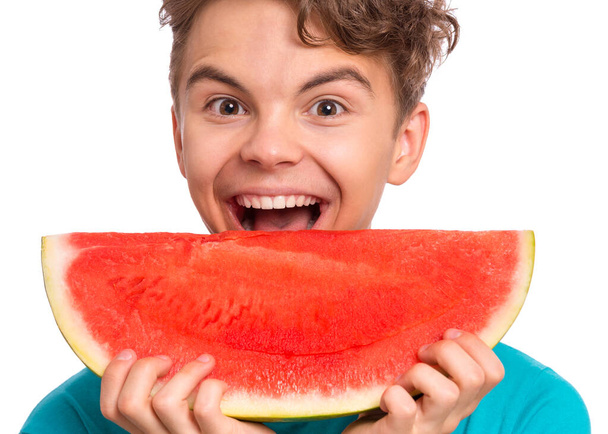 Portrait of teen boy eating ripe juicy watermelon and smiling. Cute caucasian young teenager, isolated on white background. Funny happy child bites slice of red watermelon and looking at camera. - Zdjęcie, obraz