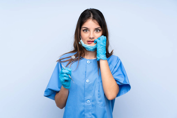 Женщина-дантист держит инструменты на изолированном синем фоне нервничает и боится
 - Фото, изображение