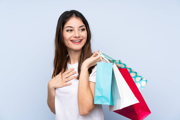 Genç esmer kadın izole edilmiş mavi arka planda alışveriş torbaları tutuyor ve gülümsüyor. - Fotoğraf, Görsel