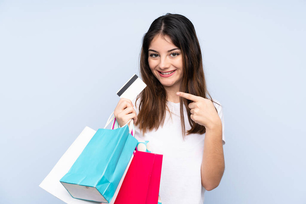 Jeune femme brune sur fond bleu isolé tenant des sacs à provisions et une carte de crédit - Photo, image