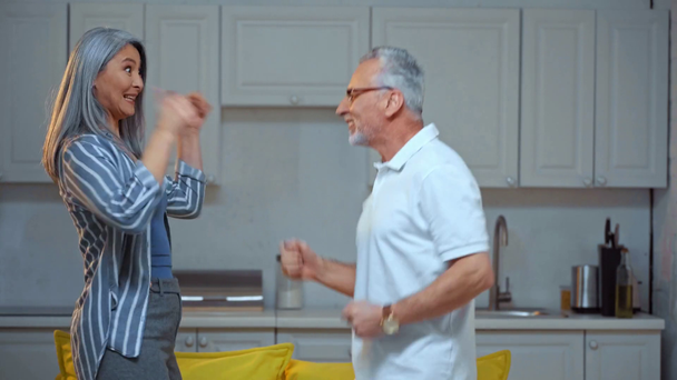 happy senior and interracial couple dancing at home - Кадри, відео