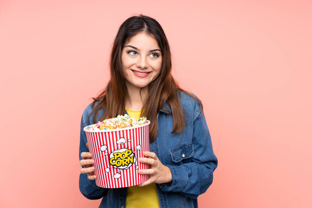 Young brunette woman over isolated pink background holding a big bucket of popcorns - Photo, image