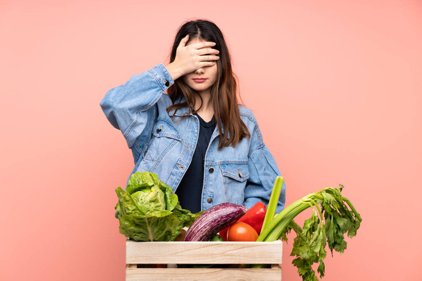 若い農家の女性が手で目を覆う新鮮な野菜でいっぱいのバスケットを持っています - 写真・画像