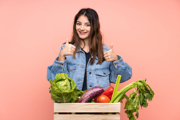 Joven campesina sosteniendo una cesta llena de verduras frescas dando un gesto de pulgar hacia arriba - Foto, imagen