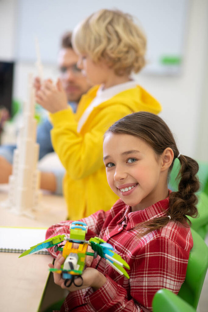 Girl holding buildable bird and smiling, boy and teacher building tower - Photo, image