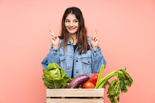Young farmer woman holding a basket full of fresh vegetables with fingers crossing - Foto, Bild