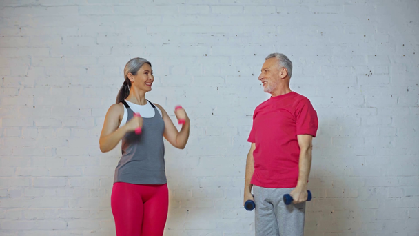 feliz pareja sénior e interracial haciendo ejercicio con pesas
  - Imágenes, Vídeo