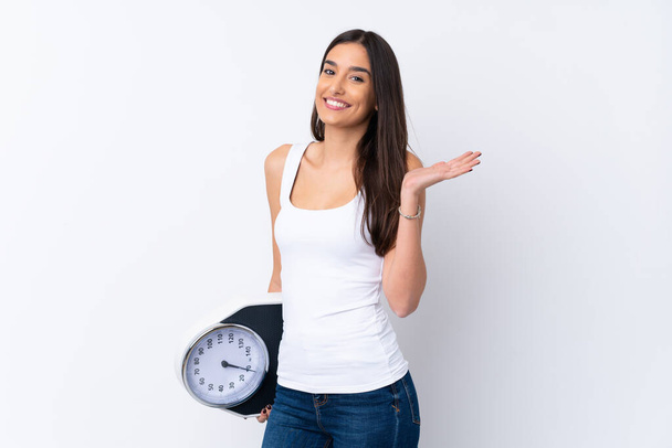Young brunette woman over isolated white background with weighing machine - Foto, Bild