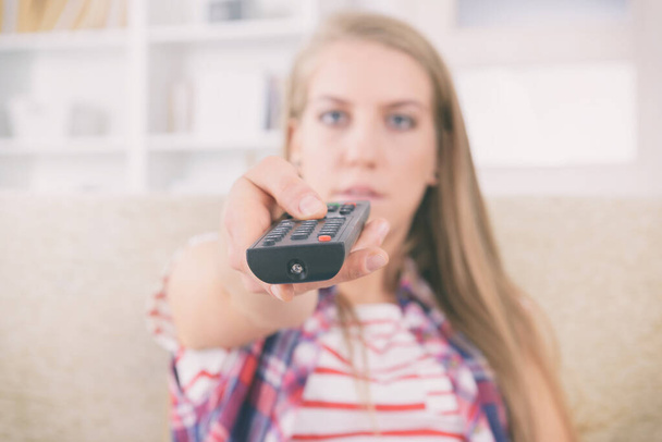Beautiful young woman holding tv remote control and changing TV channels - Foto, afbeelding