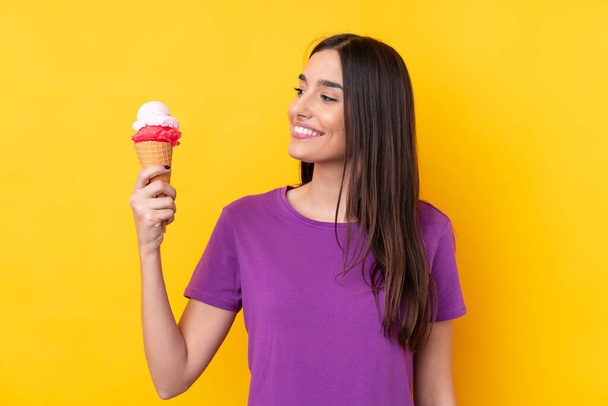 Молода брюнетка з корнетним морозивом над ізольованим жовтим тлом з щасливим виразом
 - Фото, зображення