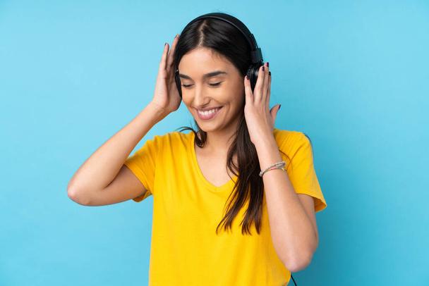 jonge brunette vrouw over geïsoleerde blauwe achtergrond luisteren muziek - Foto, afbeelding