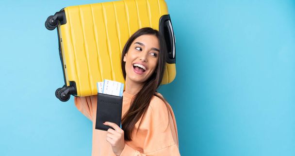 Young brunette woman over isolated blue background in vacation with suitcase and passport - Fotoğraf, Görsel