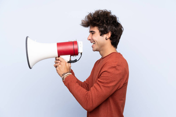 Young caucasian man over isolated blue background shouting through a megaphone - Photo, Image