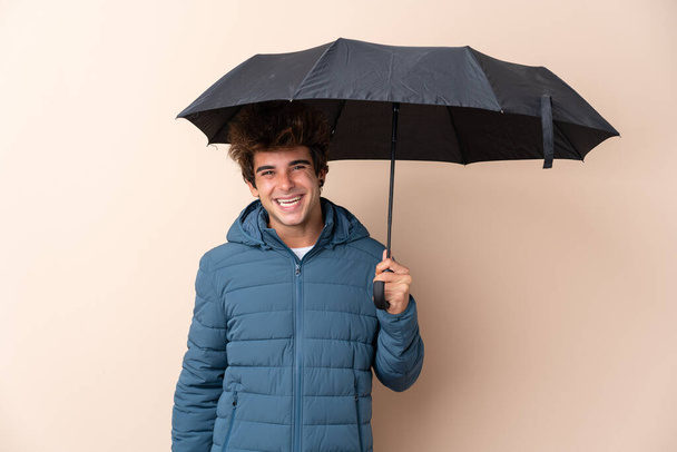 Mann hält Regenschirm über isoliertem Hintergrund und lächelt viel - Foto, Bild