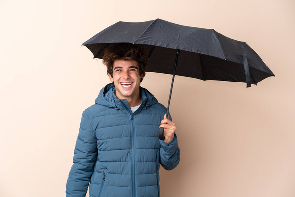 Homem segurando um guarda-chuva sobre fundo isolado com surpresa e expressão facial chocada
 - Foto, Imagem