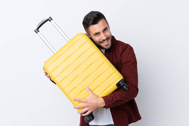 Νεαρός όμορφος άντρας πάνω από απομονωμένο λευκό φόντο σε διακοπές με ταξιδιωτική βαλίτσα - Φωτογραφία, εικόνα