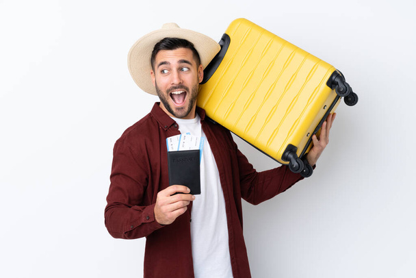 Mladý pohledný muž přes izolované bílé pozadí v dovolené s kufrem a pasem - Fotografie, Obrázek