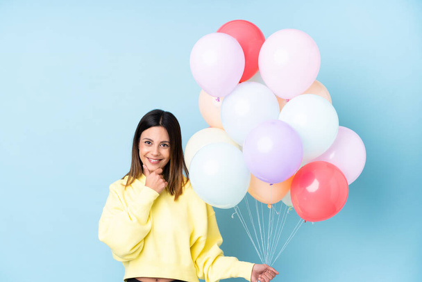 Frau hält Luftballons auf einer Party vor isoliertem blauen Hintergrund und lacht - Foto, Bild