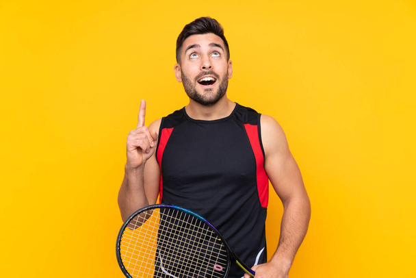 Jogador de tênis homem sobre a parede amarela isolada apontando para uma grande ideia
 - Foto, Imagem